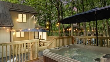 A wooden deck with a hot tub, string lights, and a covered area.