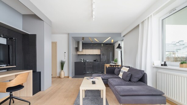 Una sala moderna con un sofá gris, una mesa de centro de madera y un televisor sobre un escritorio.