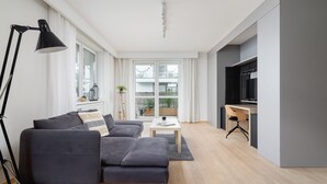 Una sala de estar moderna con un sofá gris, una mesita blanca y un televisor sobre un escritorio.