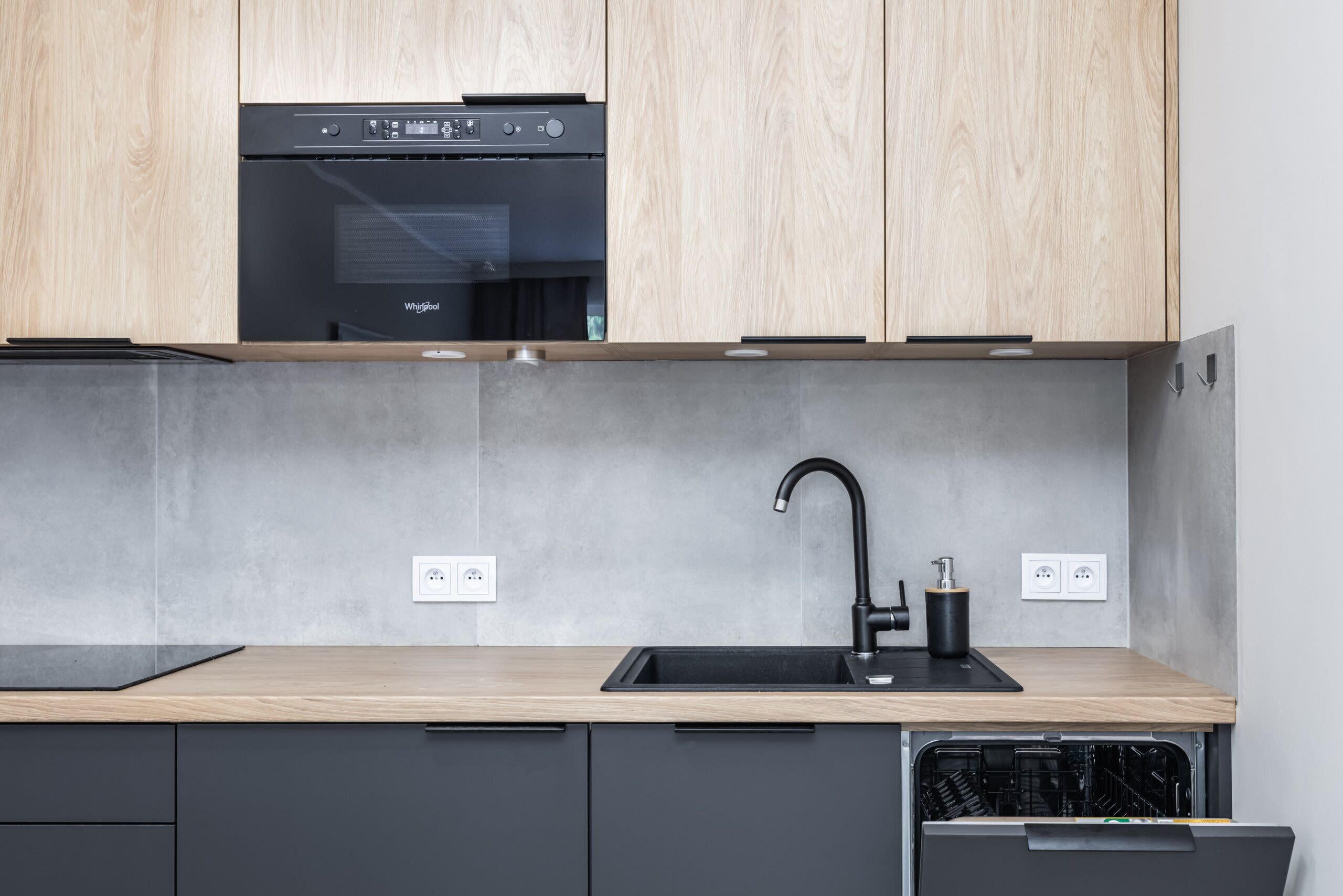 A modern kitchen with a built-in dishwasher, a black faucet, and a wooden countertop.