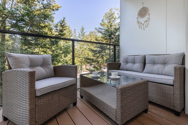 Un balcon agrémenté de meubles en osier, d’une table en verre et d’une décoration en forme d’attrape-rêves.