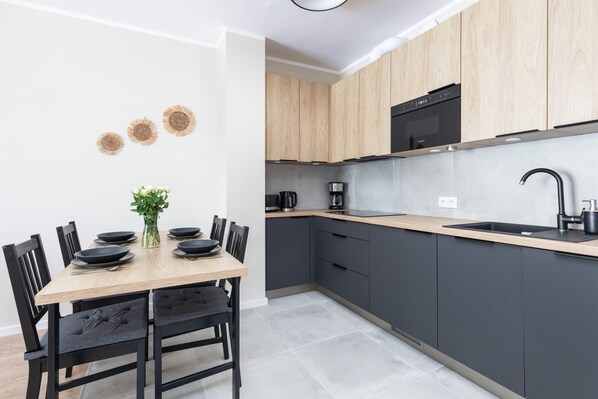 A modern kitchen with a wooden dining table, black chairs, and a black sink. - Stylish Apartment in Dziwnów | SPA (Dziwnów)