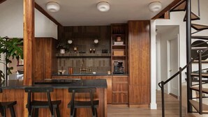 A modern kitchen with wooden cabinetry, a central island with bar stools, and a staircase with a metal railing. - Canyon Grove - Secluded lake retreat (Garfield)