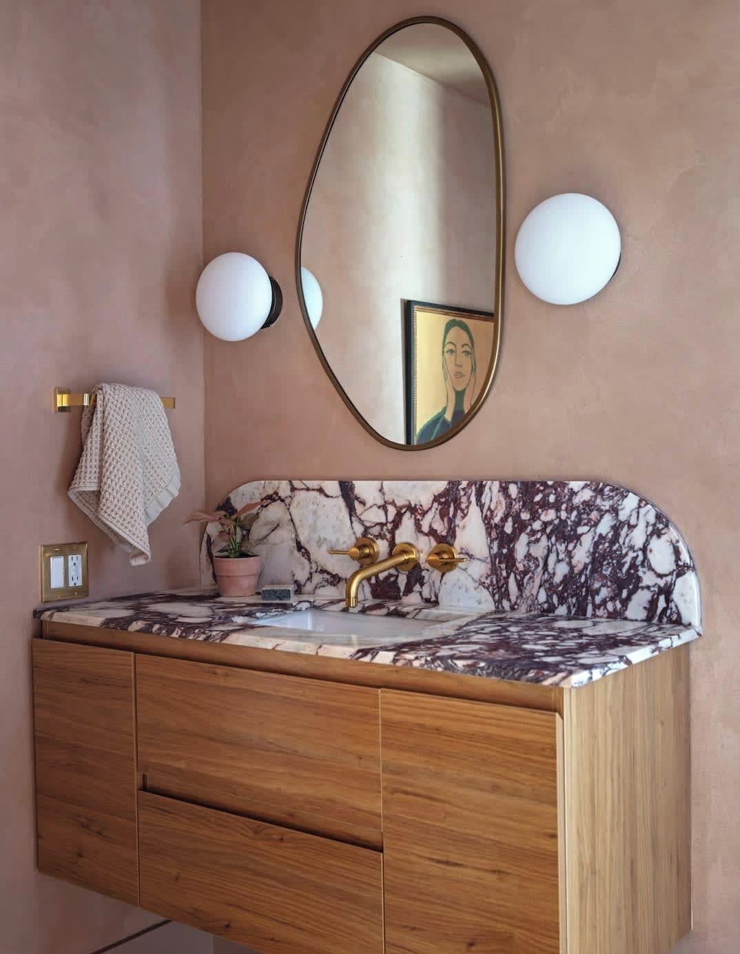 A bathroom with a marble sink, wooden vanity, gold fixtures, and a large mirror.