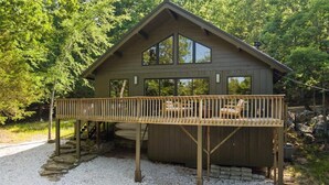 A wooden cabin with a deck, surrounded by trees.