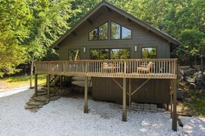 A wooden cabin with a deck, surrounded by trees.