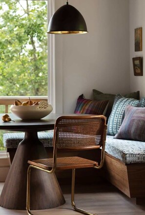 Un rincón acogedor con una silla de madera y una mesa, un cuenco de peras y una lámpara colgante negra.