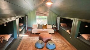A room with bunk beds, a central ottoman, and a sofa with pillows.