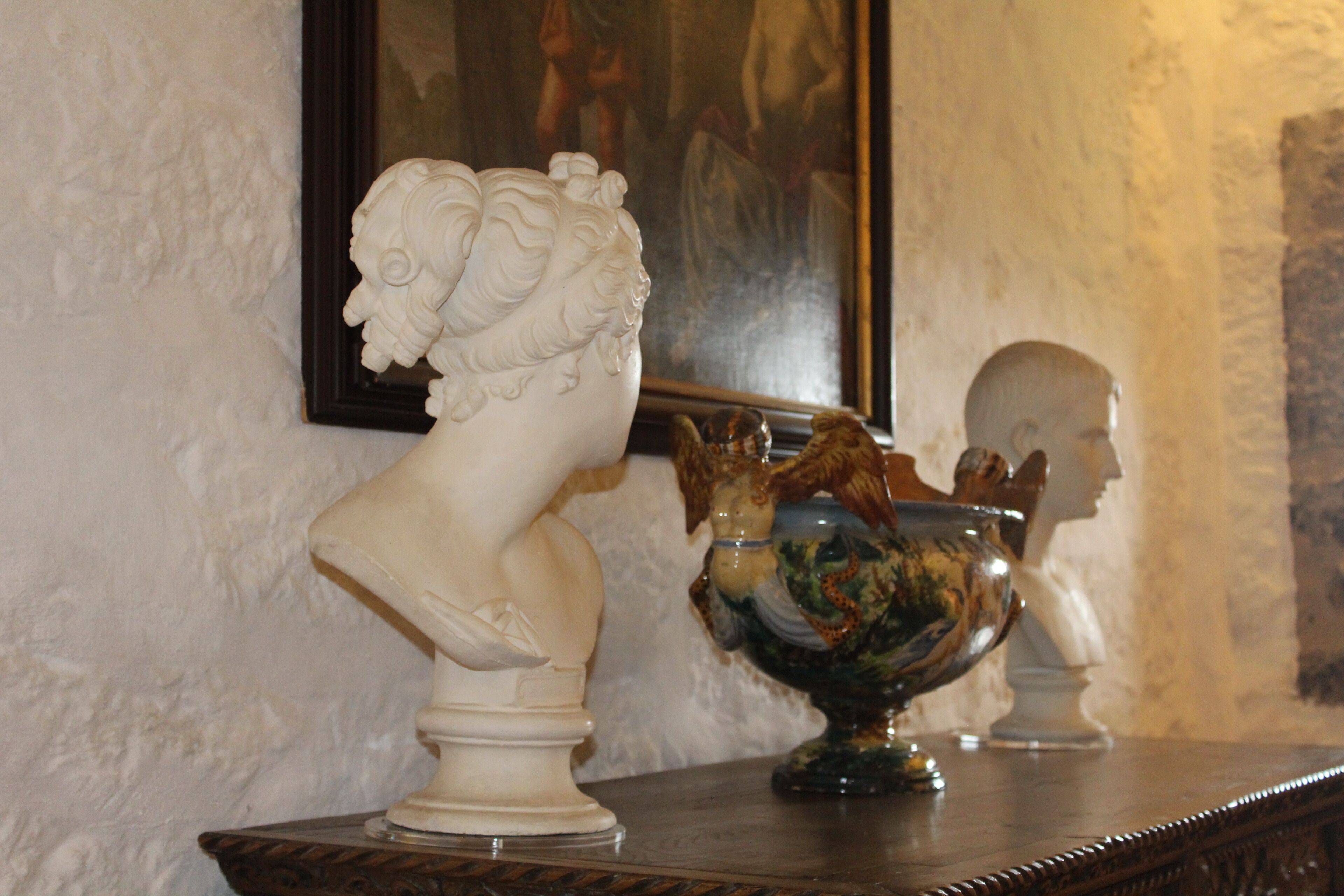 A bust sculpture on a pedestal, a decorative bowl, and a framed painting on the wall.