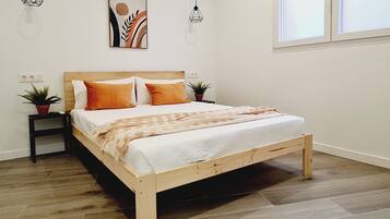 Un dormitorio con una cama de madera, dos mesitas de noche, una planta en maceta, una obra de arte colgada en la pared y una ventana con persianas.