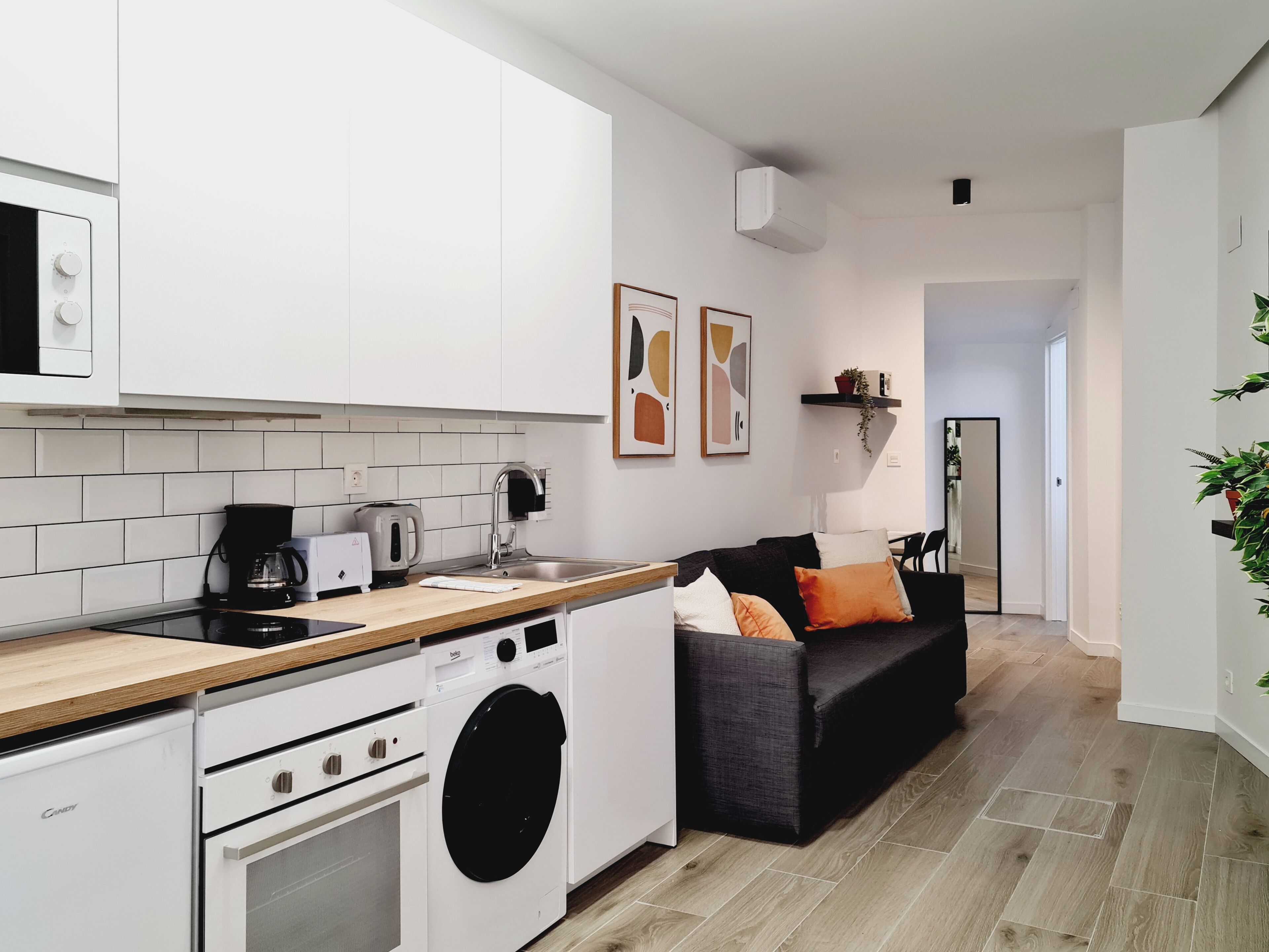 A modern kitchen with white cabinets, a built-in washing machine, and a wooden countertop.