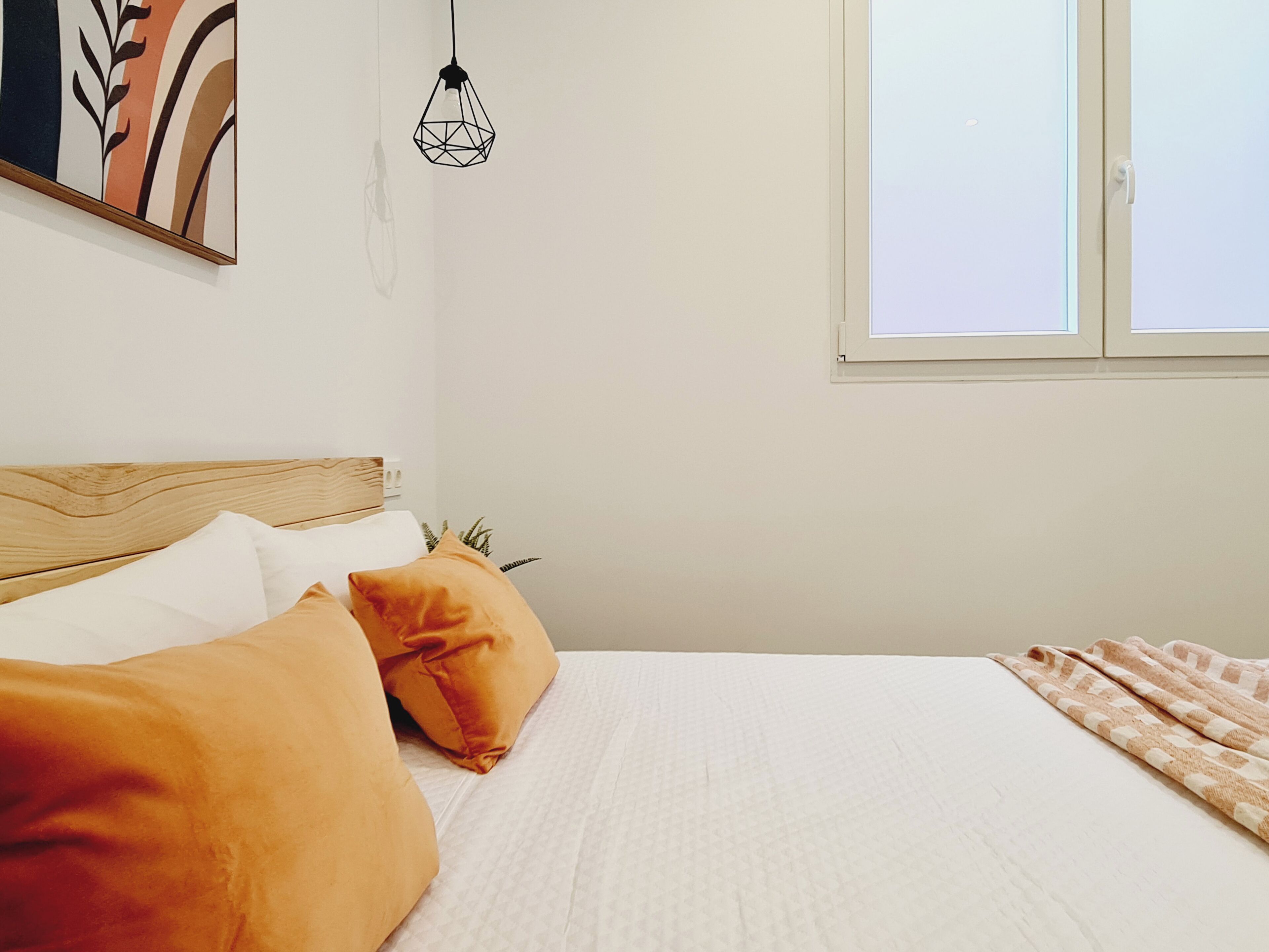 Ein Schlafzimmer mit Holz-Kopfstück, weißer Bettwäsche und einem Fenster mit Jalousien.