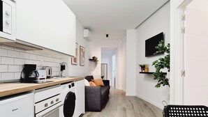 Een moderne keuken met witte apparaten, een houten aanrechtblad en een grijze bank in de woonkamer.