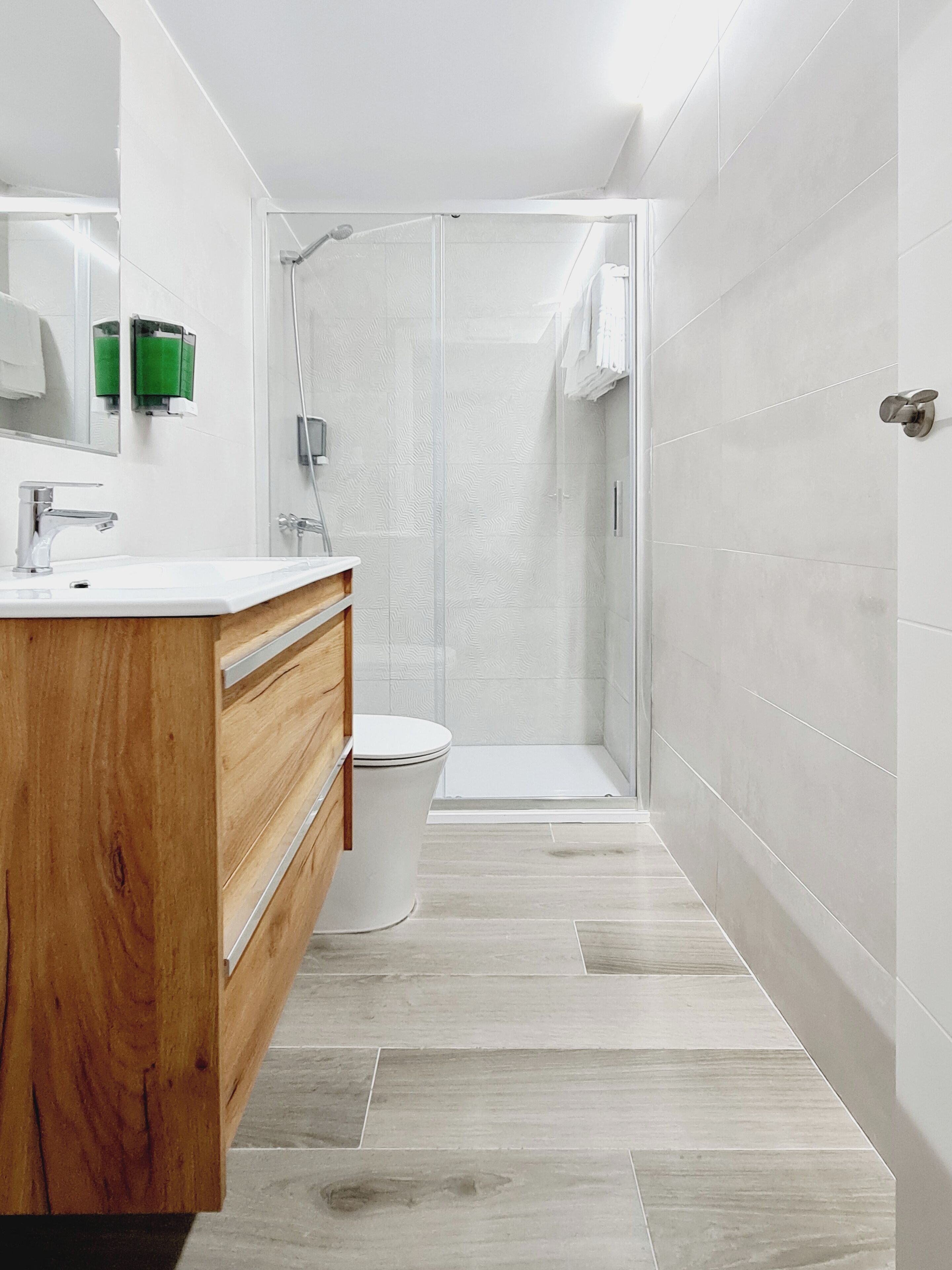 Un baño moderno con tocador de madera, inodoro y ducha con cerramiento de vidrio.