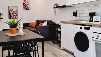 Una cucina moderna con lavatrice, un'area pranzo con tavolo e sedie, e un salotto con divano e cuscini.