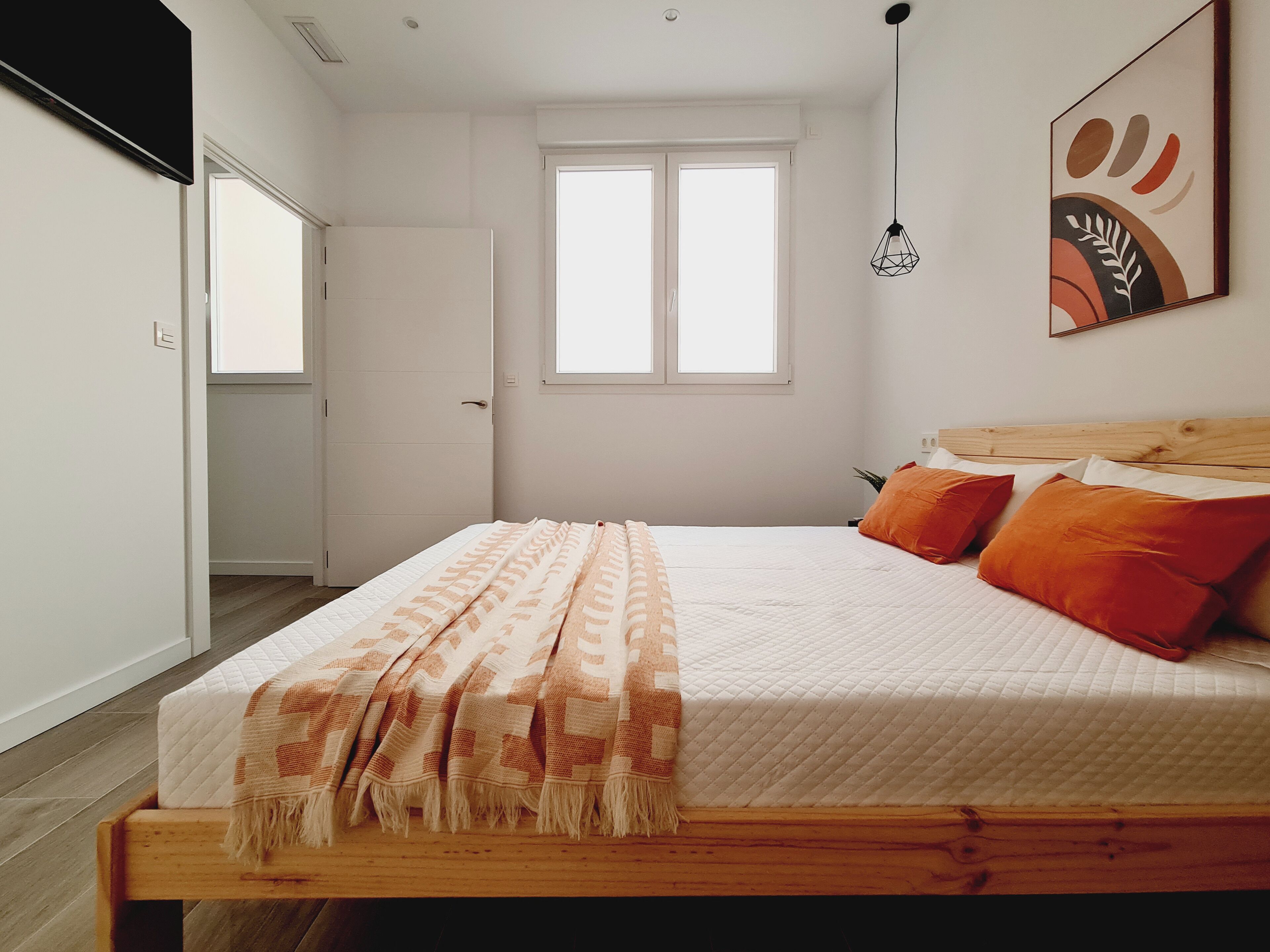Un dormitorio con una cama, cabecera de madera, una ventana y una lámpara fijada a la pared.