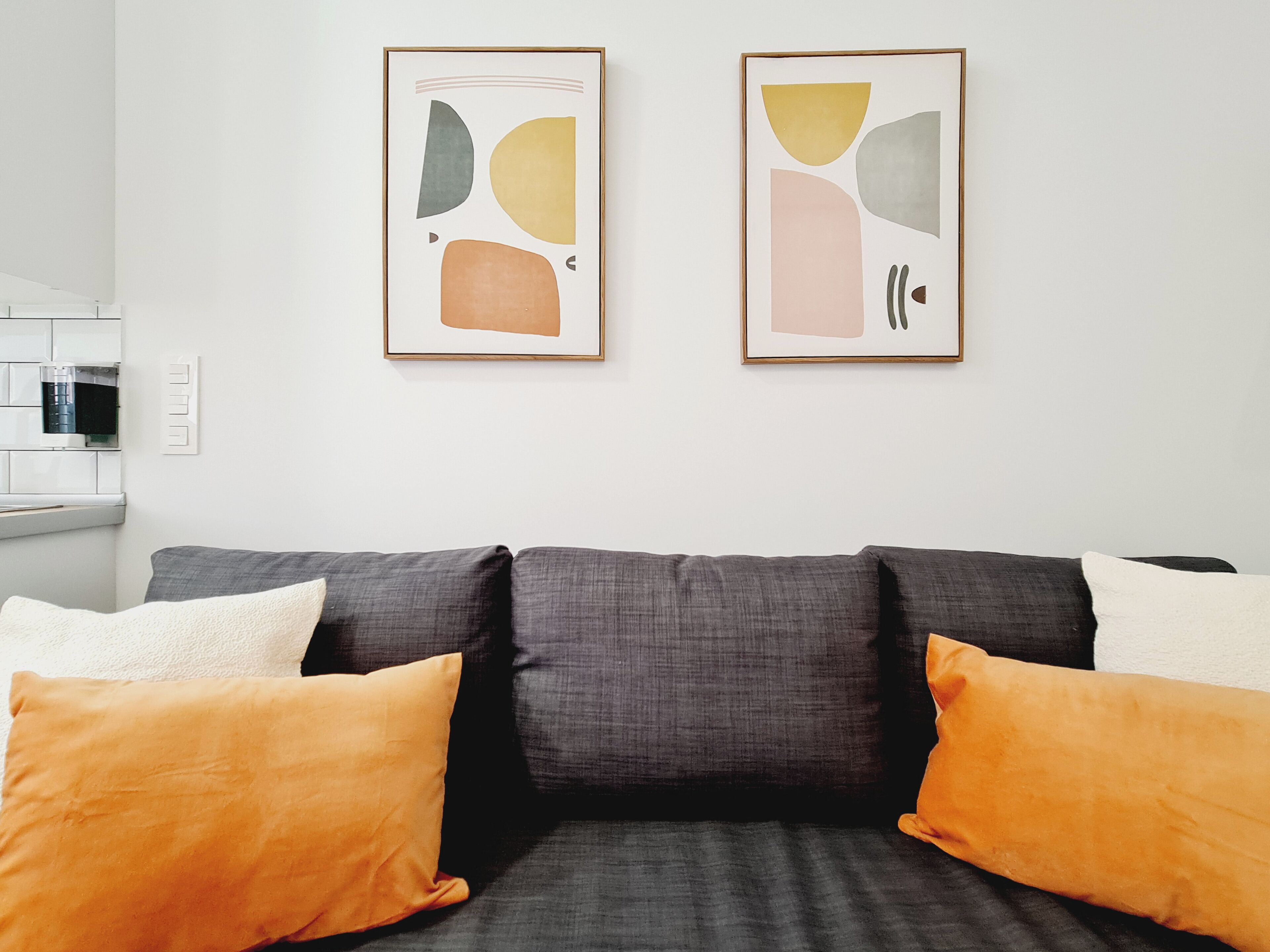 A modern living room with a grey sofa, orange cushions, and abstract artwork on the wall.