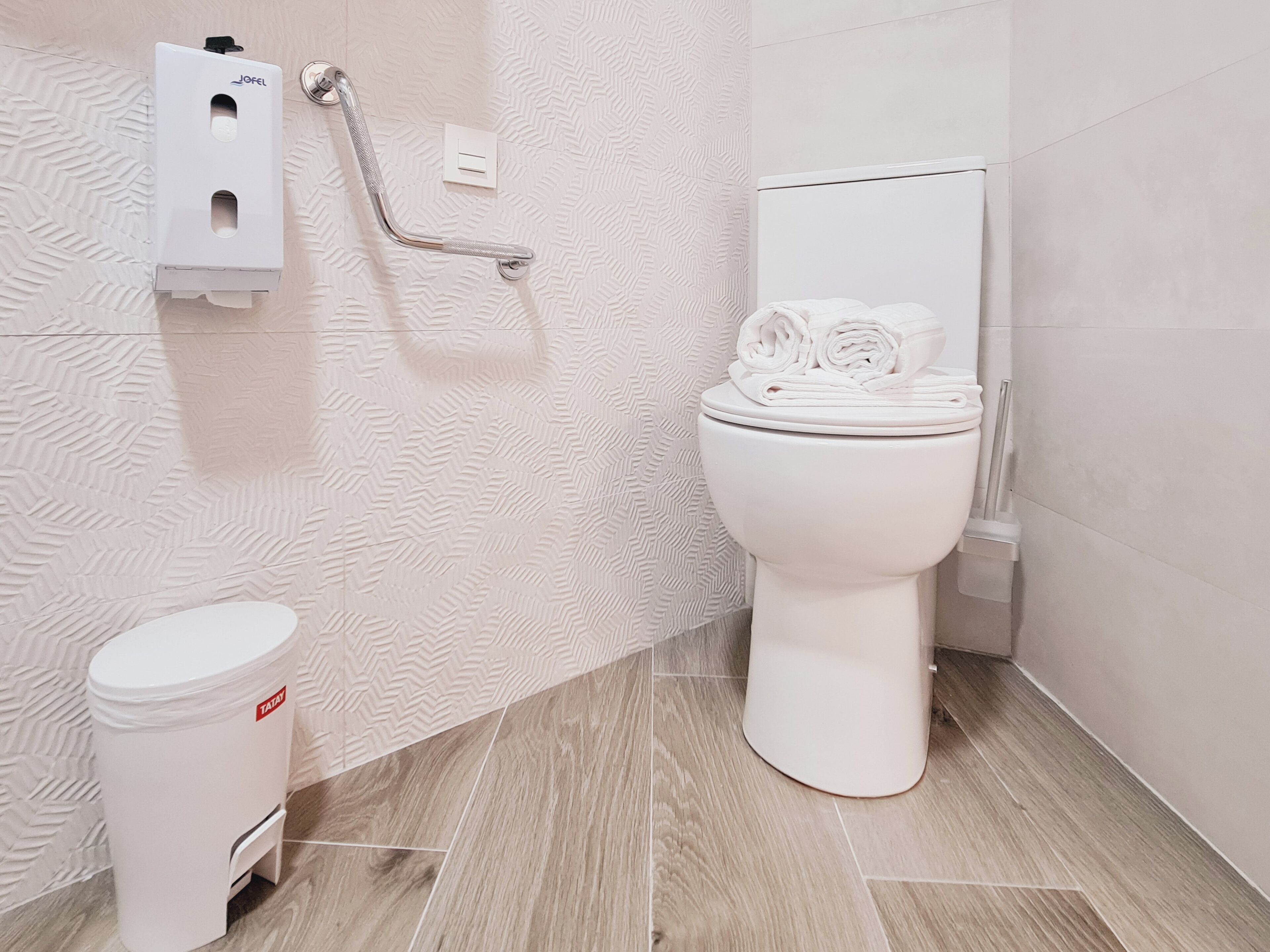 A modern bathroom with a toilet, a hand dryer, and a trash bin.