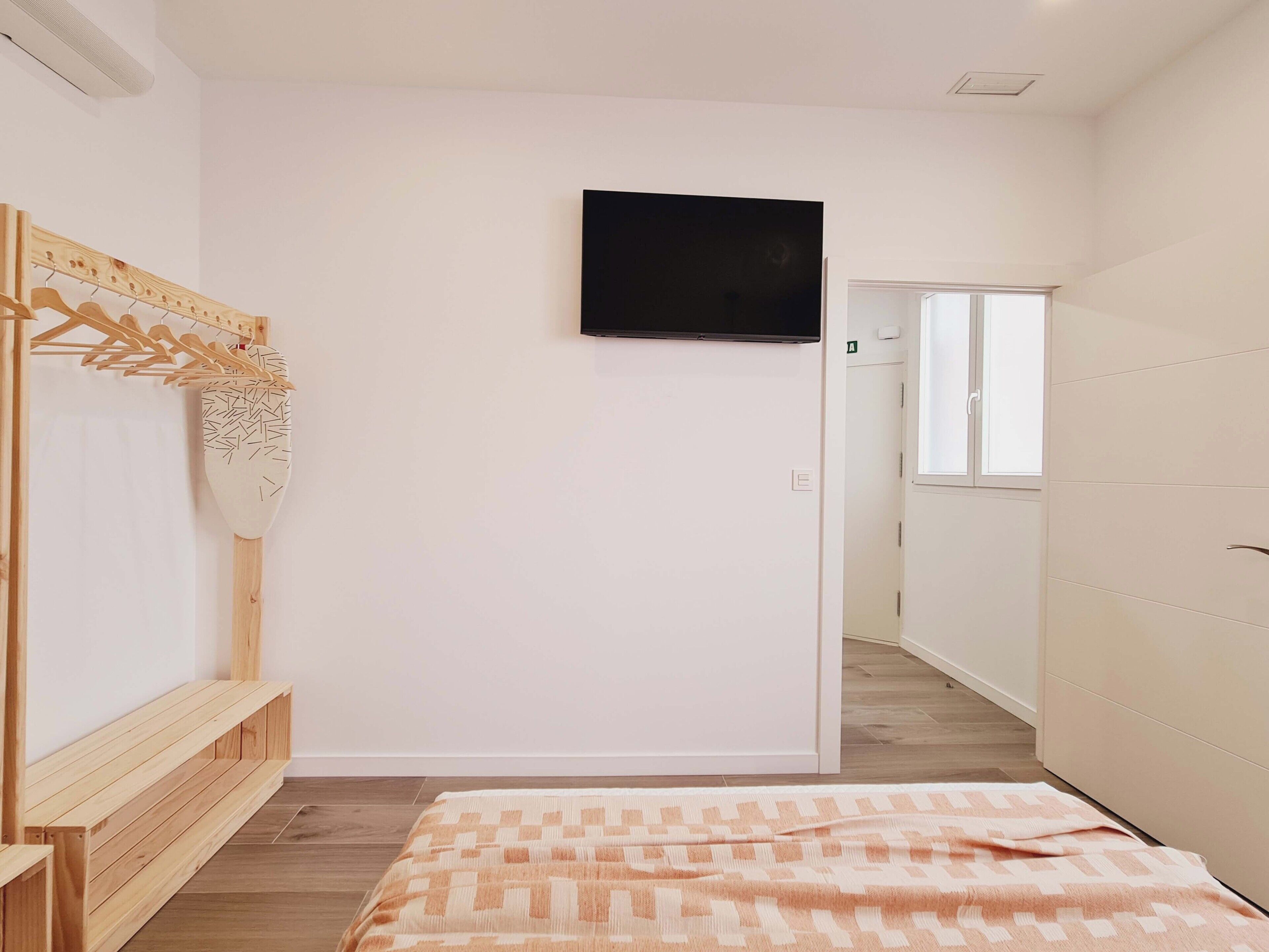 Un dormitorio con cama, un banco de madera, un televisor montado en la pared y un armario.
