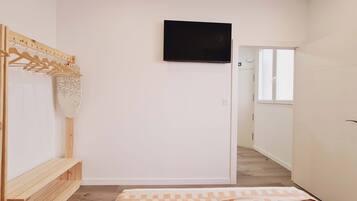 Un dormitorio con cama, un banco de madera, un televisor montado en la pared y un armario.