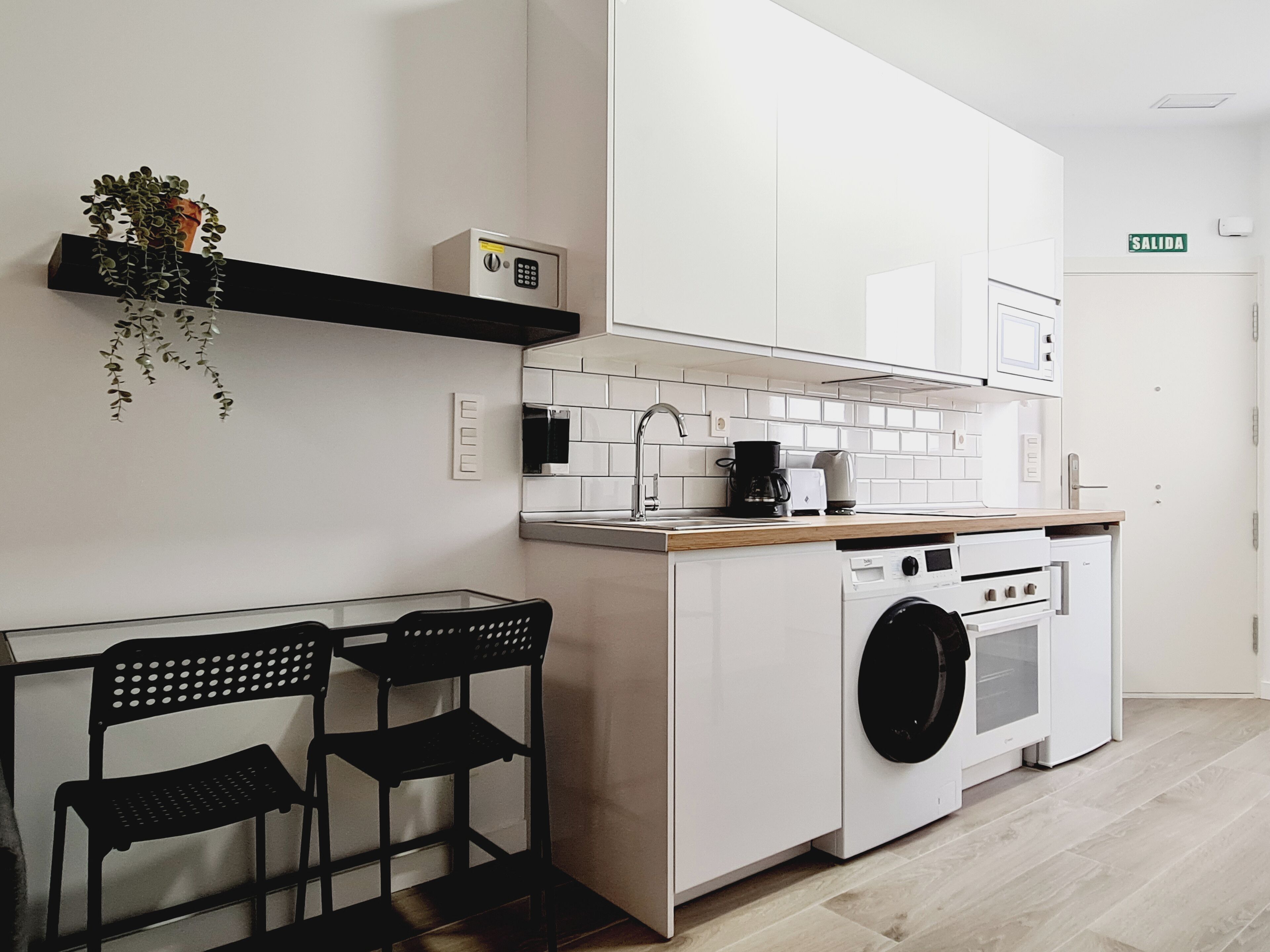 Una cocina funcional con lavadora, cafetera y un pequeño comedor con dos sillas.