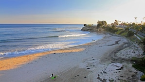 A beach with a clear sky, waves, and a few people with surfboards.