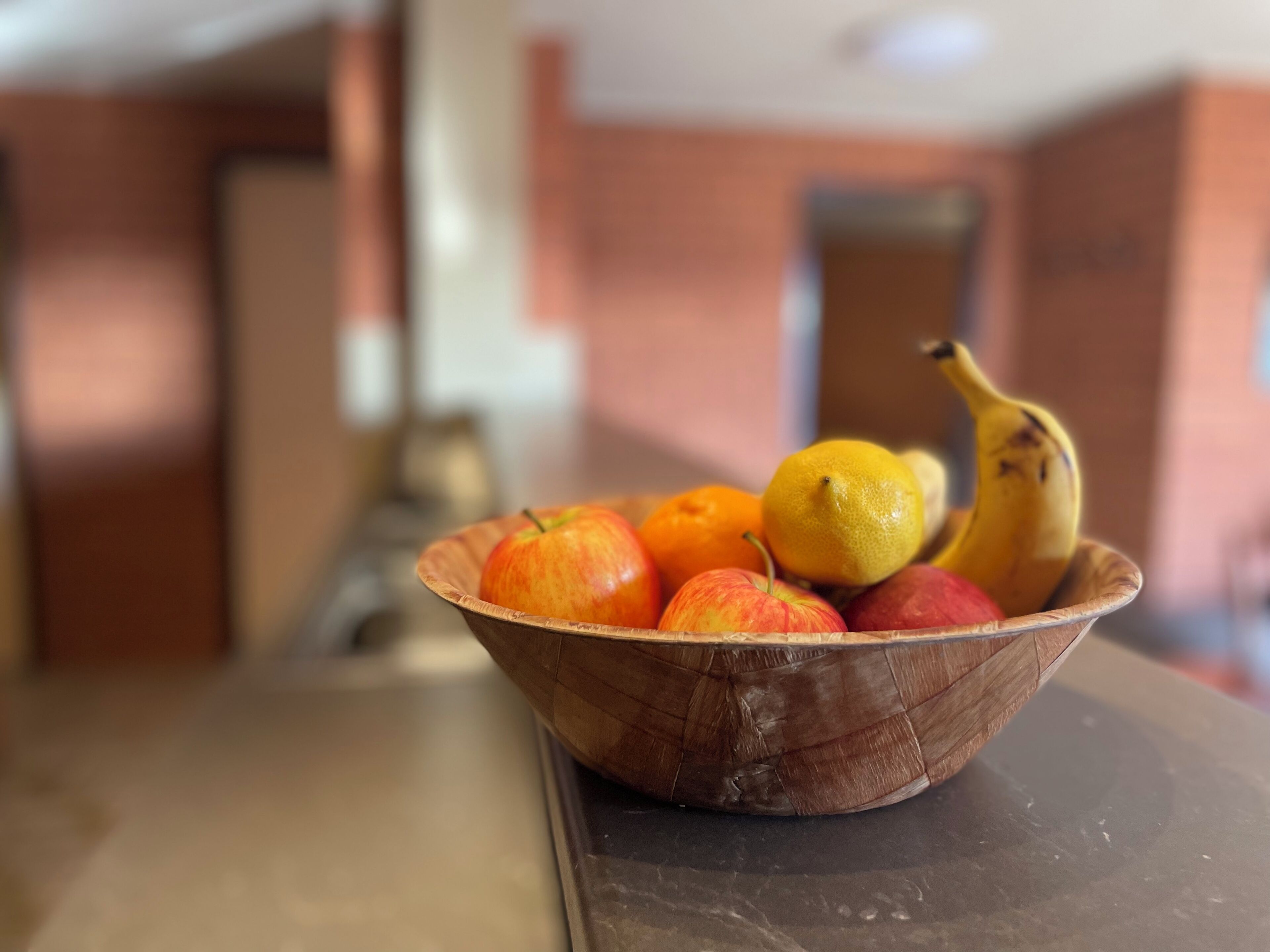En træskål med æbler, appelsiner og en banan på en køkkenbordplade.