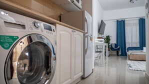 Una cuina moderna amb rentadora integrada, nevera i zona de menjador amb taula i cadires.