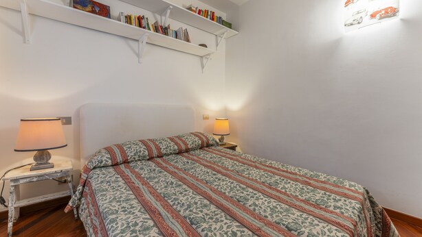 A bedroom with a bed, two bedside lamps, a nightstand, and a bookshelf with books and decorative items. - Un minuto dal mare (Bogliasco)