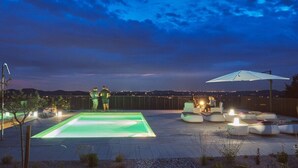 Et tagområde med swimmingpool, siddepladser og udsigt over bybilledet i skumringen.