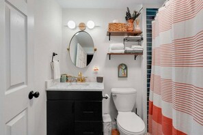 Un baño con inodoro blanco, armarios negros, espejo con iluminación, toallero y cortina de ducha a rayas.