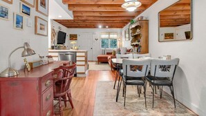 Un interno accogliente con soffitto in legno, zona pranzo con sedie, cucina con televisore e soggiorno con divano.
