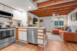 Una cocina moderna con lavavajillas, estufa y microondas. Hay una zona de comedor con sofá y ventana.