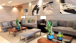 Una sala de estar moderna con un sofá gris, dos sillones, una mesita de centro y una mesita auxiliar. Hay pinturas abstractas en la pared y un letrero que dice "Staycation".