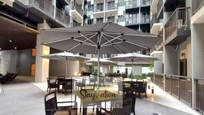 Amplia zona de estar al aire libre con varias mesas y sillas, sombrillas y una mesa central con un letrero que dice 'Staycation'.