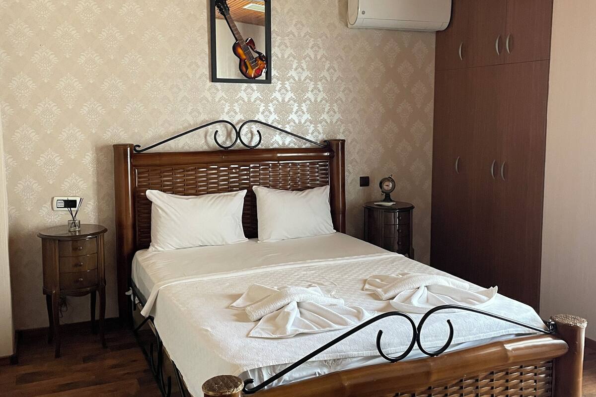 A neatly made bed with white linens, a wooden headboard, and a hanging light fixture.