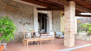 A covered outdoor patio with a stone wall, wooden furniture, and a brick pillar. - Apartment for 2/3 guests with panoramic patio, pool and Wi-Fi (Toscana)