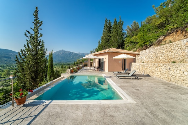 A modern villa with a swimming pool, stone walls, and a view of the mountains.