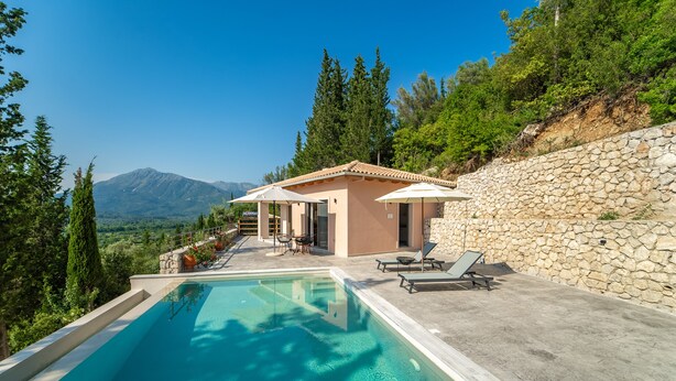 A poolside area with a stone wall, a small building, and a view of mountains. - Kipseli Villa, Overlooking Vassiliki bay (Lefkada)