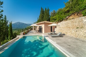 Ein Poolbereich mit Steinmauer, einem kleinen Gebäude und Blick auf Berge.