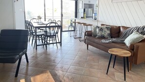 Ein geräumiger Wohnbereich mit einem braunen Ledersofa, einem Esstisch mit Stühlen und einer Küchenzeile mit Kühlschrank und Kaffeemaschine.