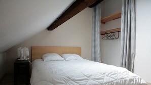 Un dormitorio con cabecera de madera, colcha blanca acolchada y mesita de noche con un objeto blanco encima.