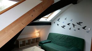 Habitación estilo loft con techo inclinado, un sofá verde, una mesita y una pared decorada con calcomanías de pájaros.