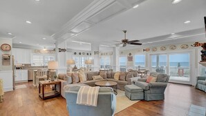 A spacious living room with a large sectional sofa, a dining area with a table and chairs, and a kitchen in the background. - Oceanfront Mega Estate | Private Pool, Sleeps 25, Game Rooms & Decks (Isle of Palms)
