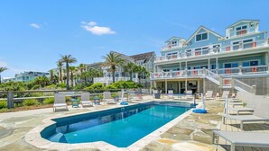 A swimming pool with lounge chairs, a stone deck, and a multi-story building with balconies. - Oceanfront Mega Estate | Private Pool, Sleeps 25, Game Rooms & Decks (Isle of Palms)