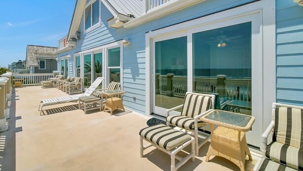 A beachfront property with a covered patio area featuring striped lounge chairs and a glass table. - Oceanfront Mega Estate | Private Pool, Sleeps 25, Game Rooms & Decks (Isle of Palms)