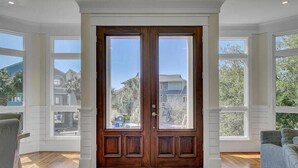 A double wooden door with glass panels, a wooden floor, and a view of houses through the windows. - Second Star | Oceanview Coastal Showpiece with Private Pool (Isle of Palms)