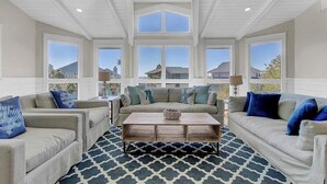 A spacious living room with a high ceiling, large windows, and a patterned rug. - Second Star | Oceanview Coastal Showpiece with Private Pool (Isle of Palms)