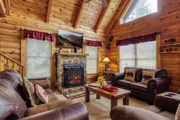A cozy log cabin interior with a fireplace, leather sofas, and a stone accent wall.