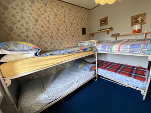 A bunk bed room with floral wallpaper, a blue carpet, and a shelf with books and a vase.